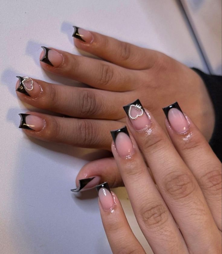 Chic Nail Design: Nude Polish with Bold Black Tips and Charming Accents.