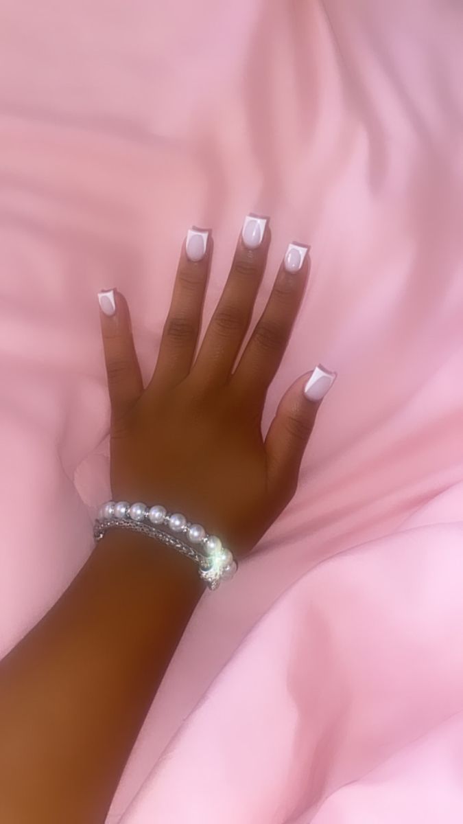 Elegant Chic Nail Design with White Square Tips and Pearl Bracelet on Soft Pink Background.