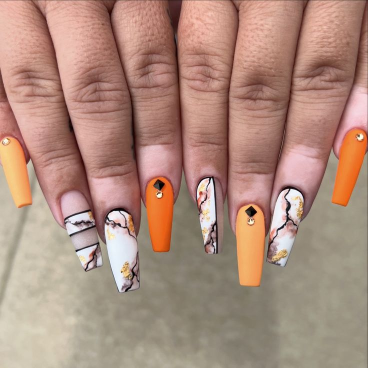 Chic Matte Orange and Marbled Nail Design with Floral and Geometric Details and Sparkling Rhinestones.