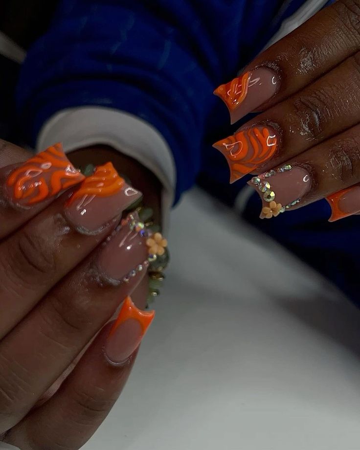 Bold Orange and Nude Nail Design with Glamorous Accents and Intricate Patterns.