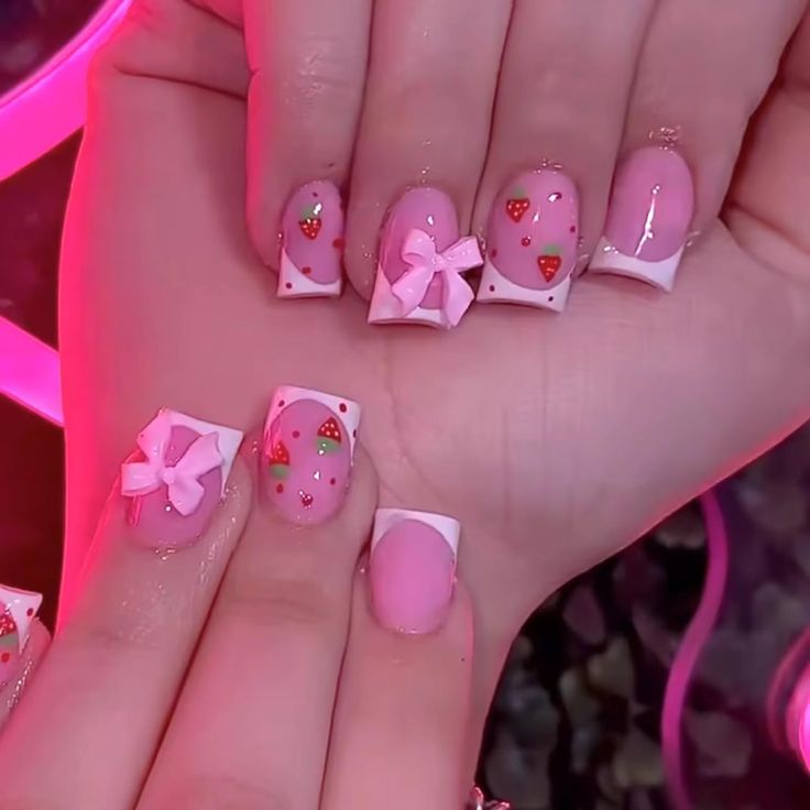 Charming Playful Nail Design: Soft Pink Base with Strawberry and Bow Embellishments and White French Tips.