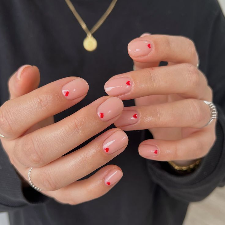 Charming Nude Nail Design with Playful Red Heart Accents for a Subtle Romantic Touch.