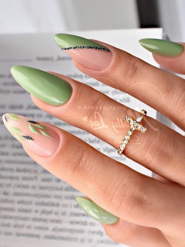 Chic Almond-Shaped Nail Design in Soft Green and Nude with Leafy Accents and Glitter Details.