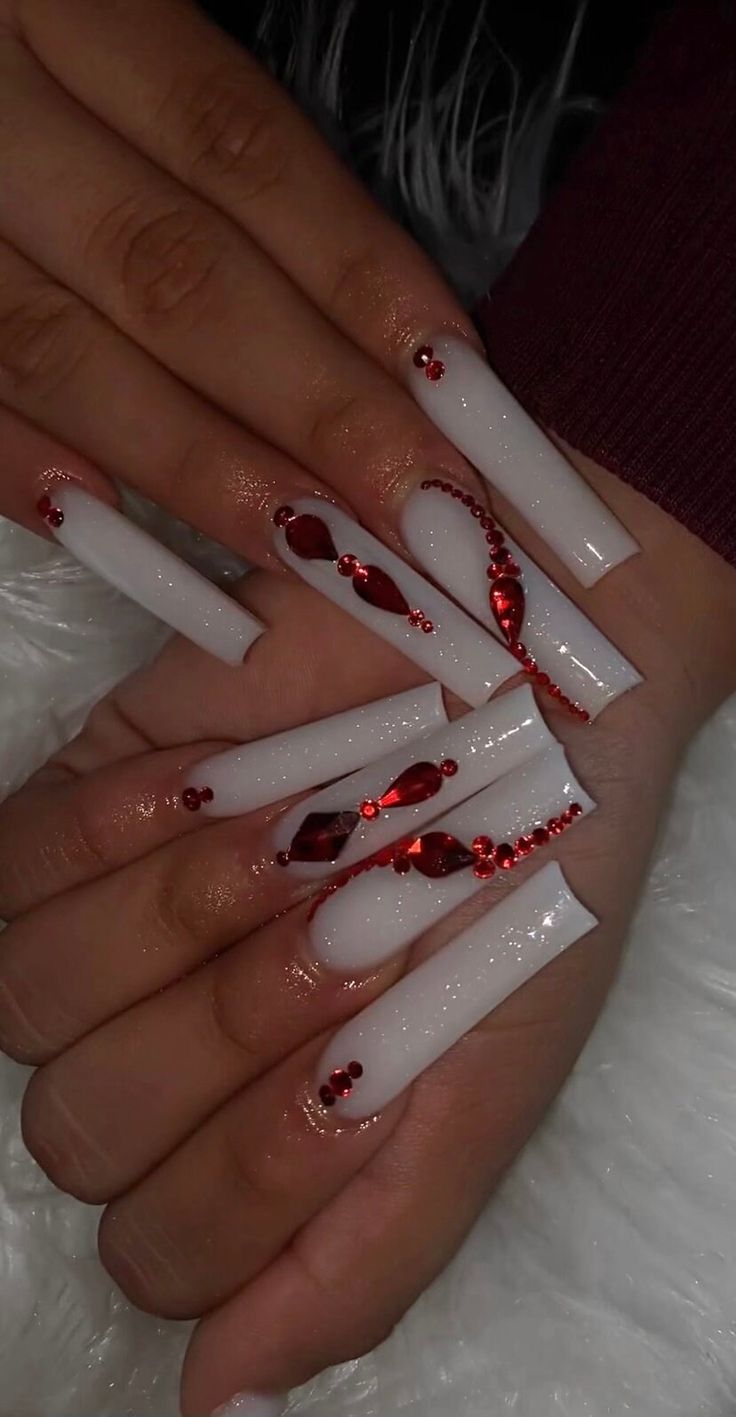 Elegant Elongated Glossy White Acrylic Nails Embellished with Vibrant Red Gems and Beads.