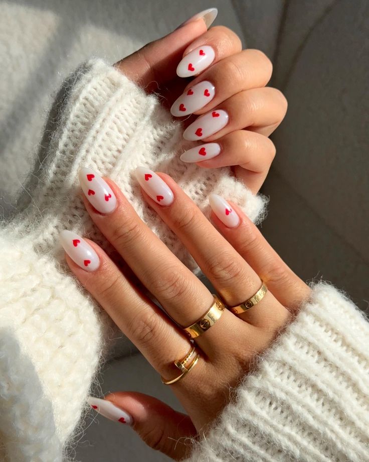 Chic Heart-Themed Nail Design with Matte White Base and Red Hearts, Perfectly Paired with a Cozy Sweater and Gold Rings.