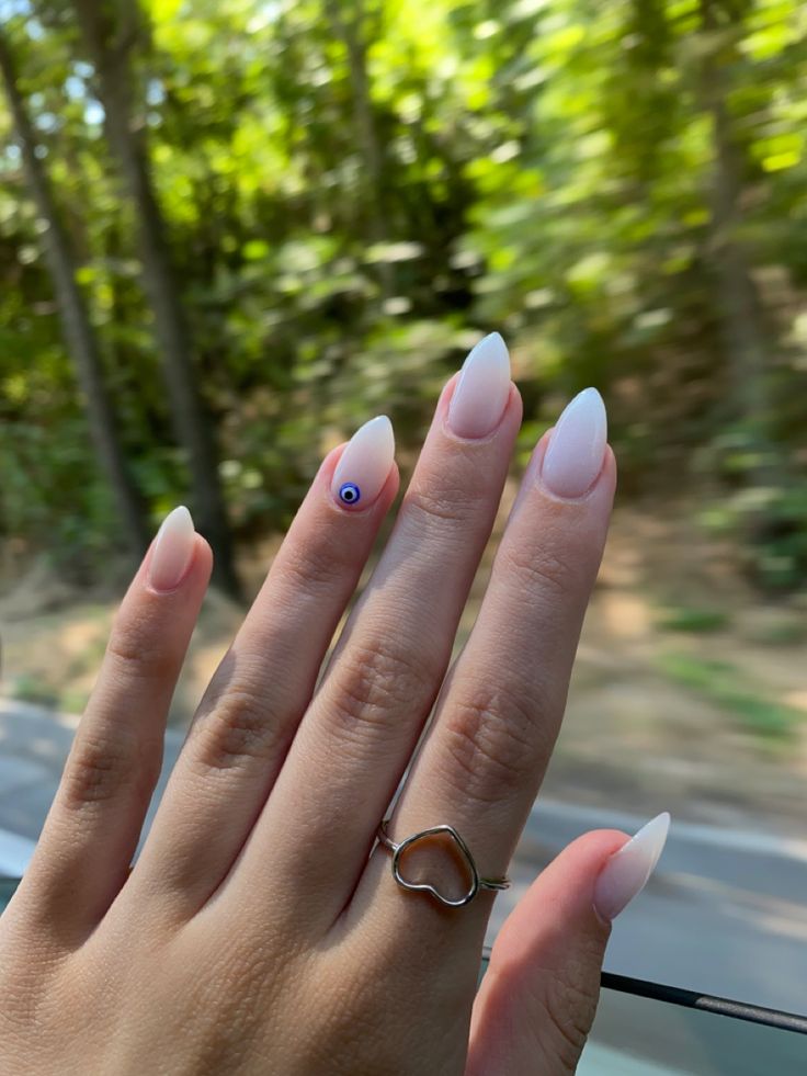 Chic Almond-Shaped Gradient Nails with Unique Blue Eye Accent and Heart-Shaped Ring.