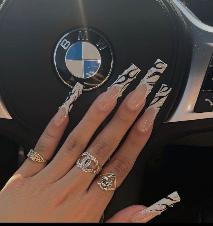 Chic Long Nails with Nude Base and Bold Black Flames, Enhanced by Elegant Rings in Sleek Car Interior.