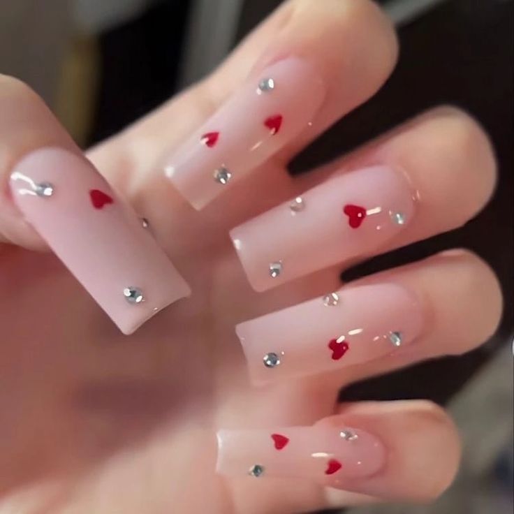 Chic Romantic Nail Design with Soft Pink Base, Red Heart Accents, and Sparkling Rhinestones.