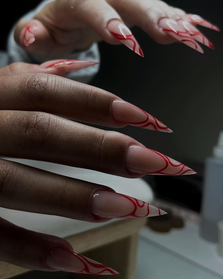 Sophisticated Stiletto Nail Design with Intricate Red Swirls on Soft Nude Base