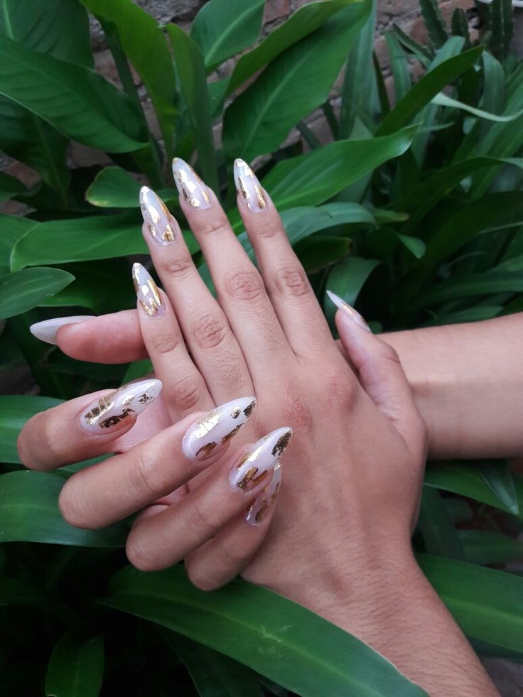 Luxurious Almond Nail Design with Nude Base and Gold Foil Accents on a Lush Green Backdrop.