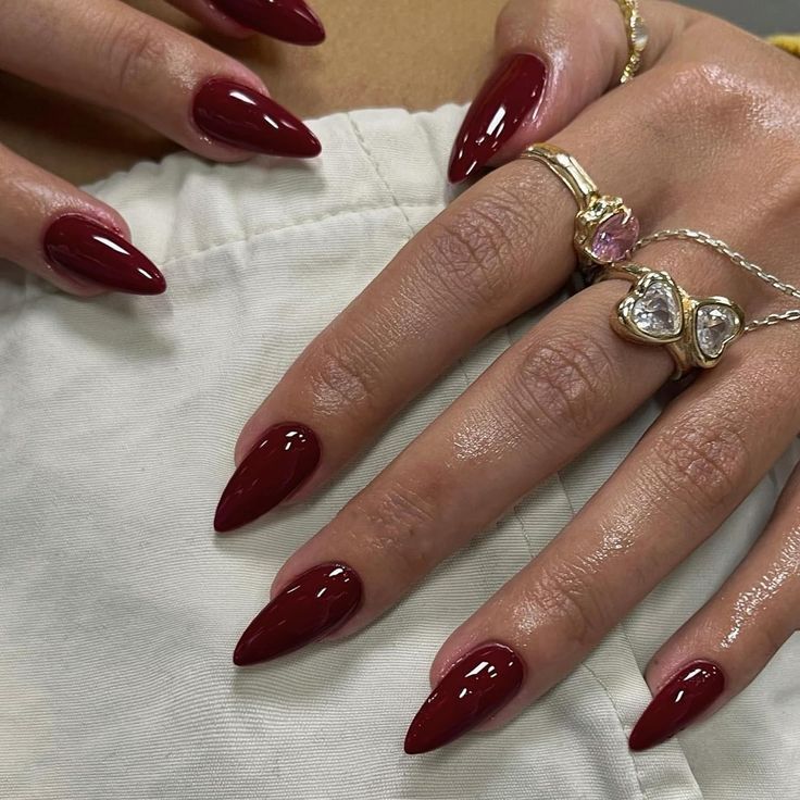 Elegant Deep Burgundy Almond-Shaped Nails Enhanced by Glossy Finish and Chic Rings.