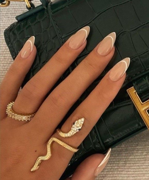 Chic Almond-Shaped Nails with Elegant Nude Polish and White Tips, Enhanced by Bold Gold Jewelry.