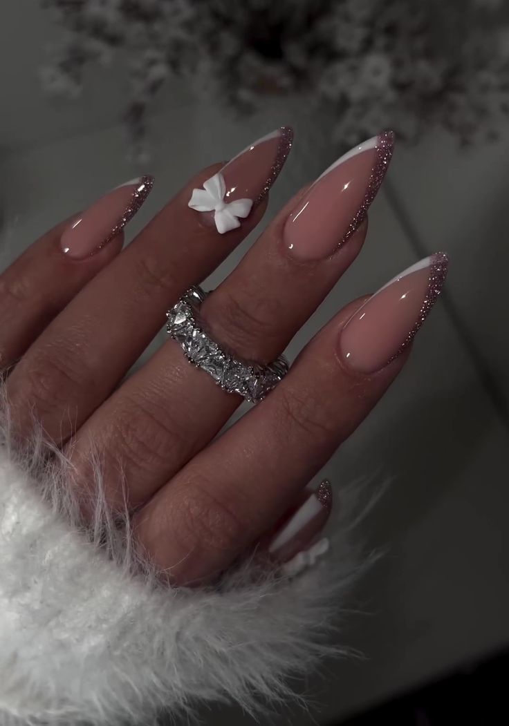 Glamorous Almond-Shaped Nails with Pink Base, Glittery Tips, and Floral Accent.