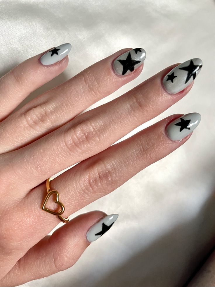 Modern Almond-Shaped Nails: Soft Gray Base with Bold Black Stars and a Charming Heart Ring.