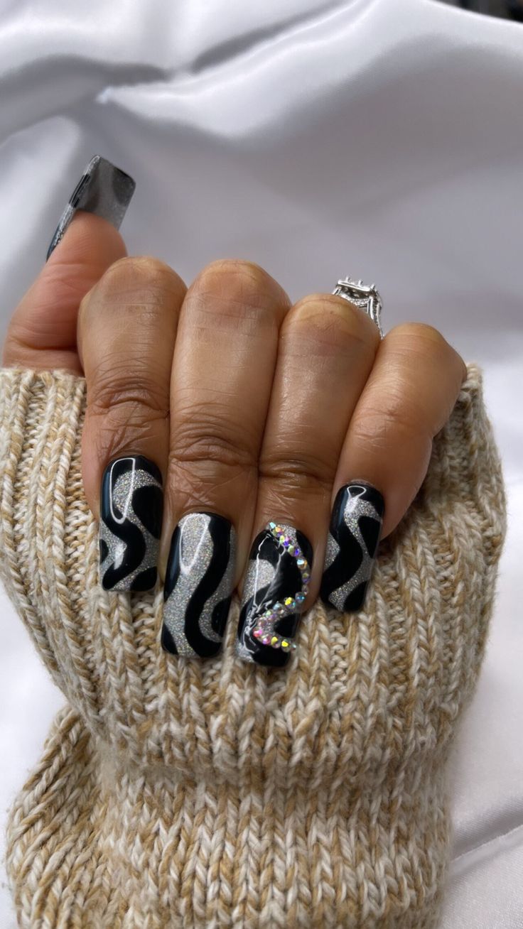 Captivating Nail Design: Bold Black Base with Wavy Silver Glitter and Glamorous Gem Accent.