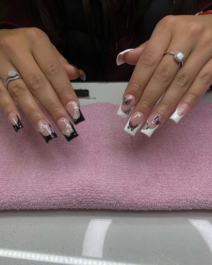 Chic Black and White Tip Nail Design with Floral Patterns on Soft Pink Background.