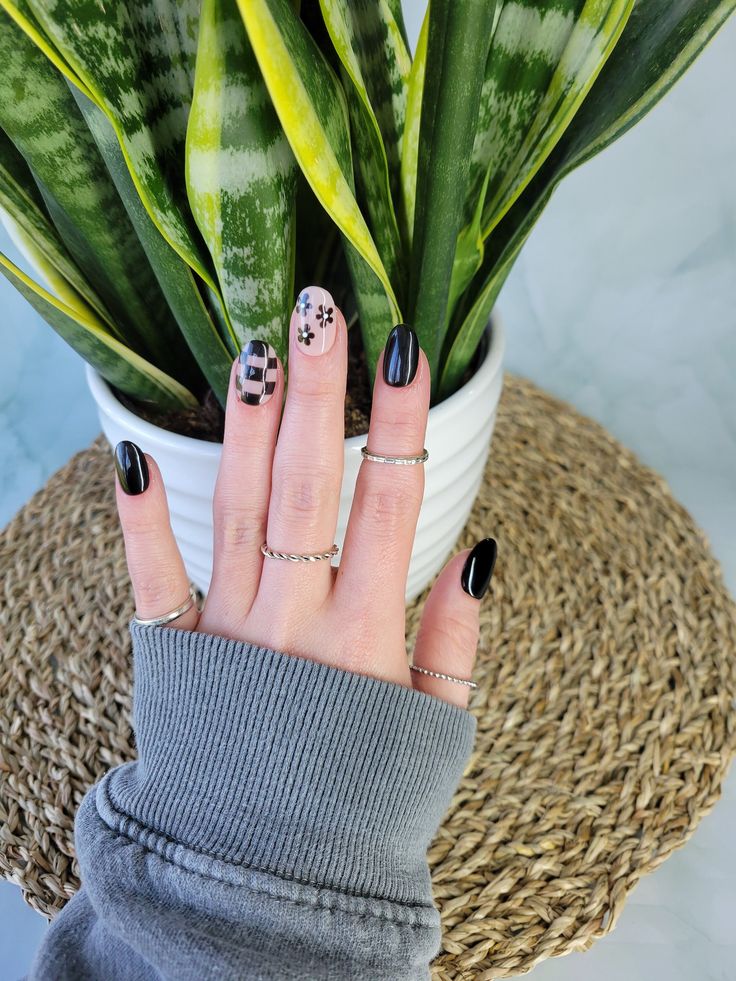 Chic Black and White Nail Design with Checkered and Floral Accents, Enhanced by Minimalist Silver Rings.