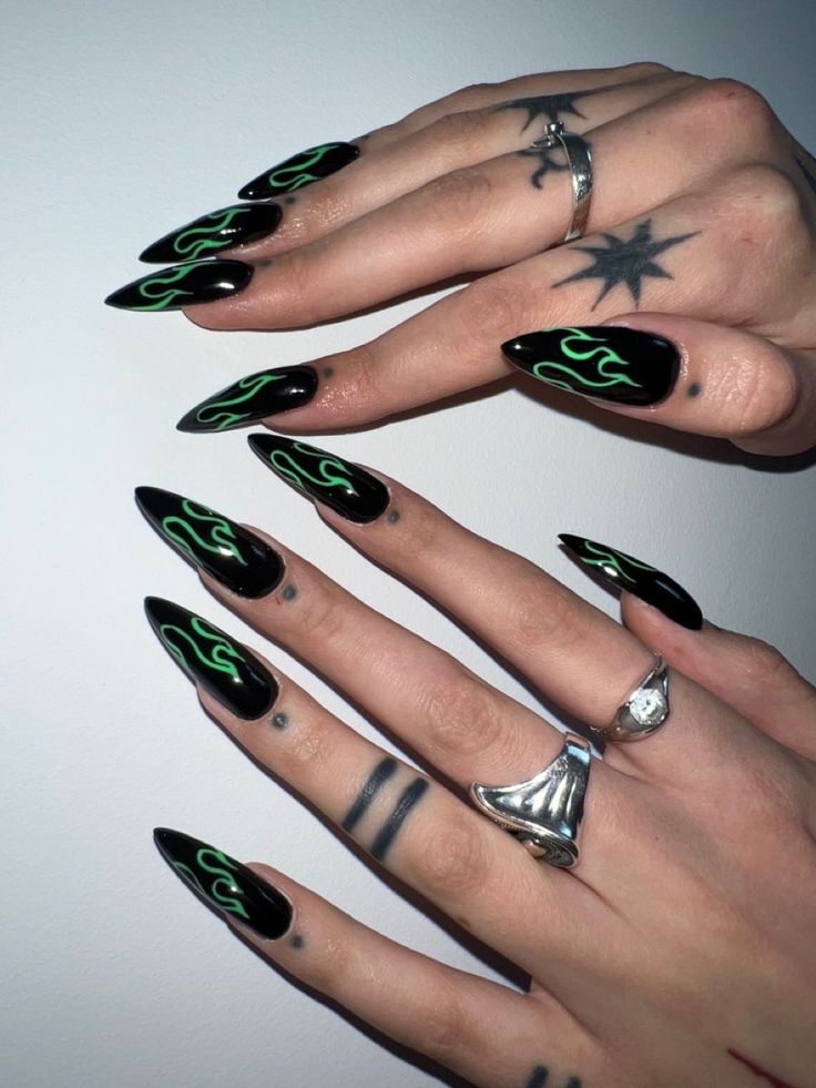 Edgy Gothic Nail Design: Glossy Black Stiletto Tips with Neon Green Flames and Silver Accents.