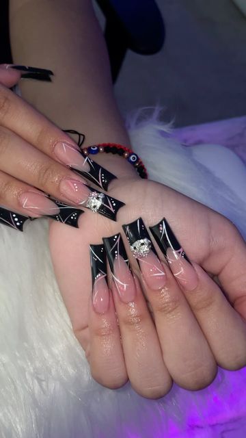 Striking Black and Nude Dramatic Nail Design with Pointed Tips, White Swirls, and Rhinestone Accents.