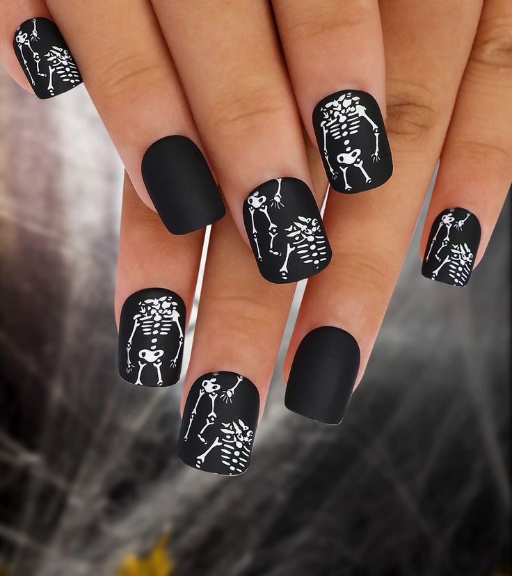 Chic Matte Black Halloween Nail Art with Playful White Skeleton Designs.