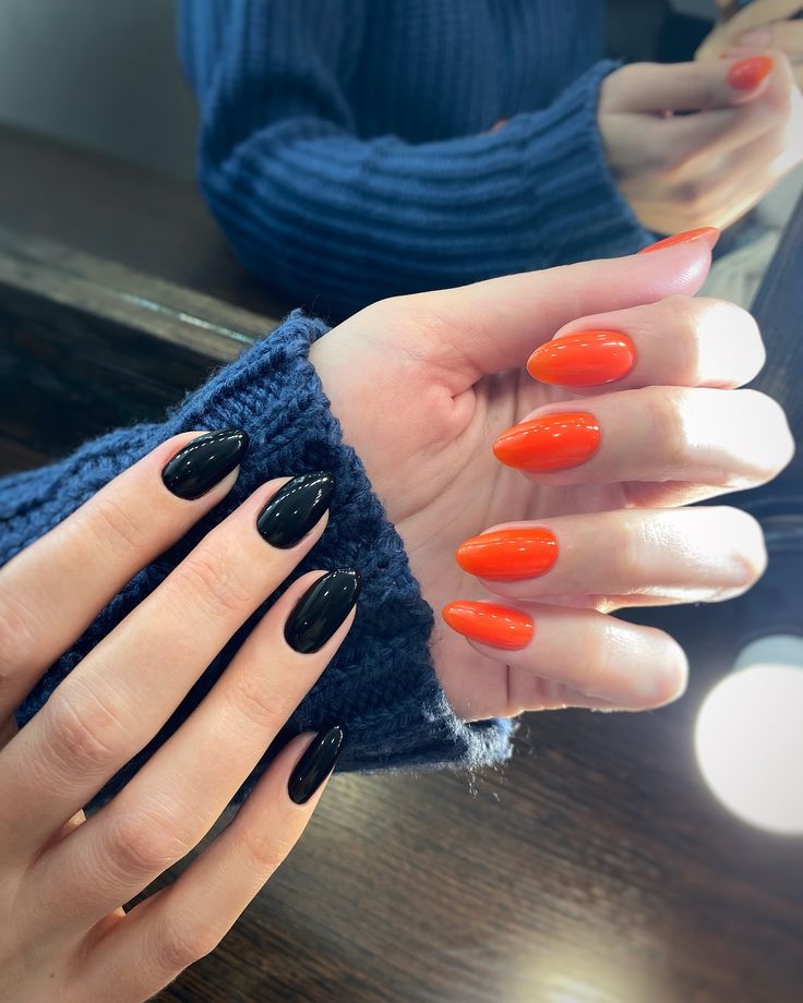 Chic Nail Design: Elegant Black Almonds Meet Vibrant Orange Ovals for a Bold Statement.