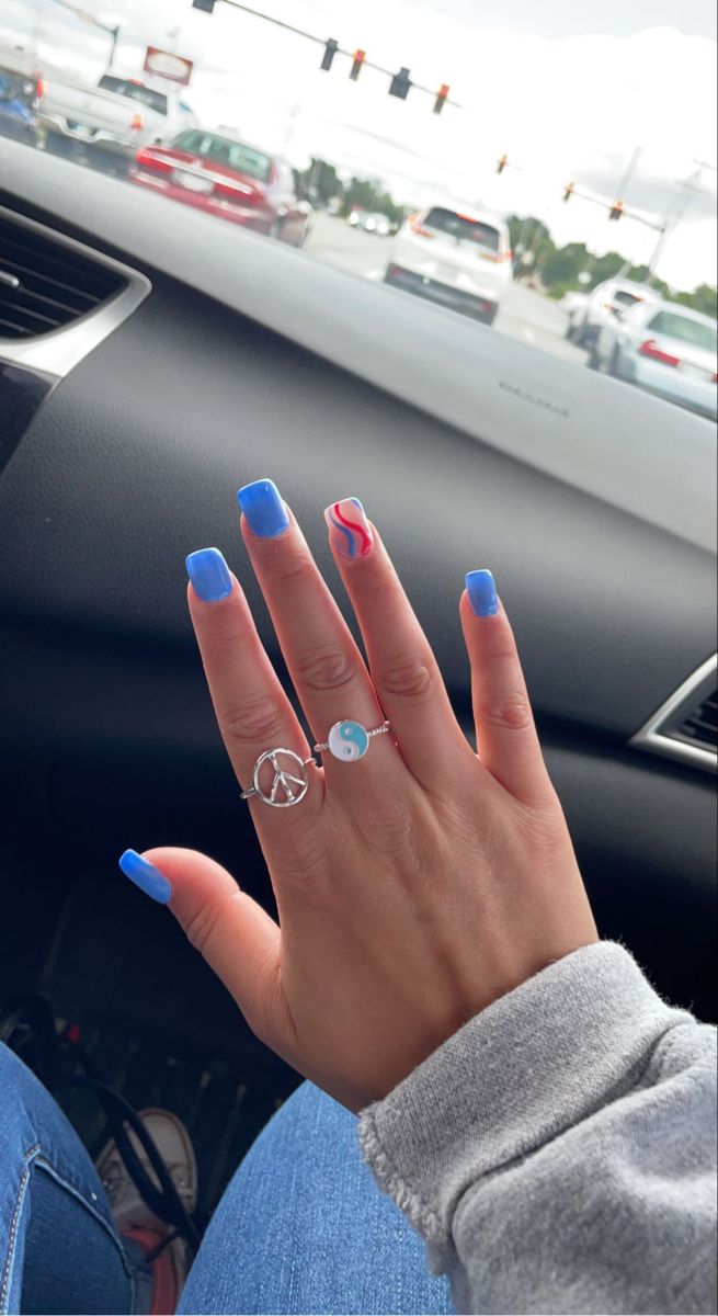 Trendy Vibrant Blue Nail Design with Glossy Finish and Artistic Pink Swirls, Enhanced by Unique Silver Rings.