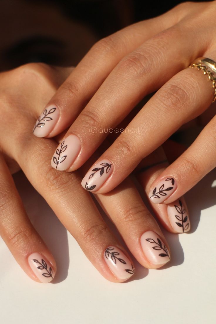 Sophisticated Nail Design: Soft Nude Base with Intricate Black Leaf Patterns.