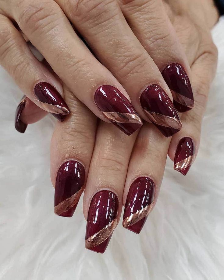 Sophisticated Burgundy Nails with Glossy and Matte Finishes Enhanced by Angled Gold Stripes.