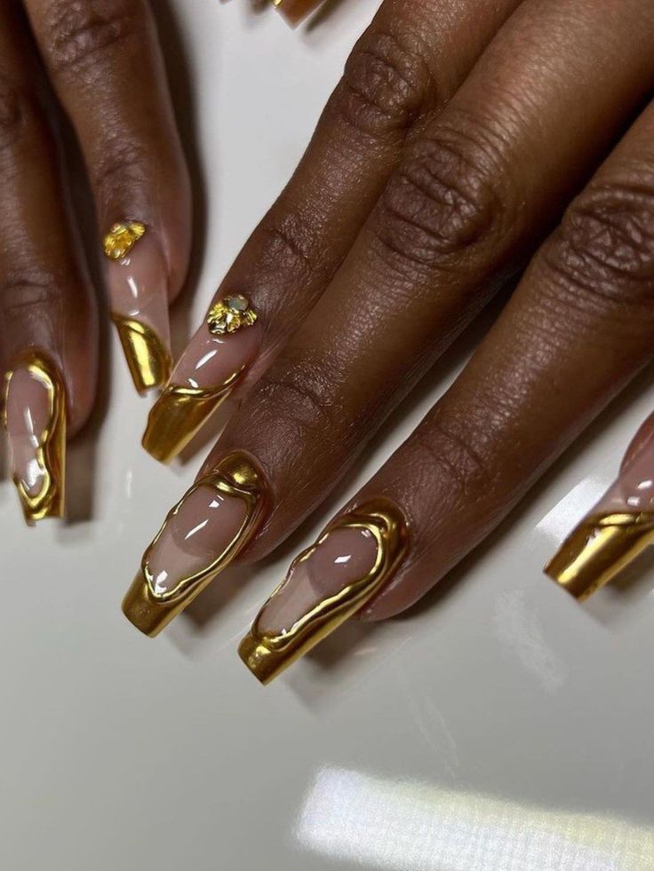 Chic Nude and Gold Nail Design with Artistic Swirls and Gem Embellishments.