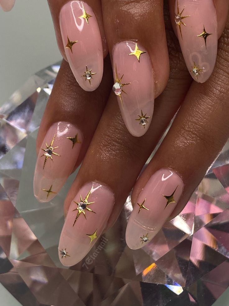 Celestial Glam: Elegant Soft Pink Nail Design with Gold Stars and Sparkling Rhinestones.