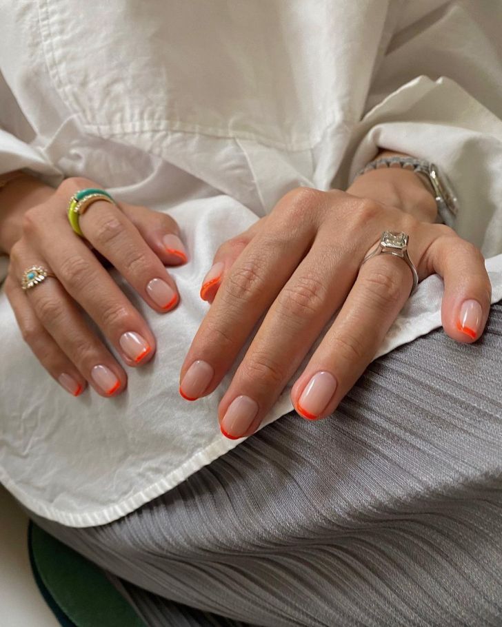 Vibrant Orange-Tipped Peachy Nude Nail Design with Elegant Ring Accents.