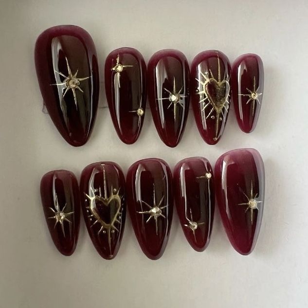 Chic Elegant Burgundy Nail Design with Intricate Gold Embellishments and Glossy Finish.