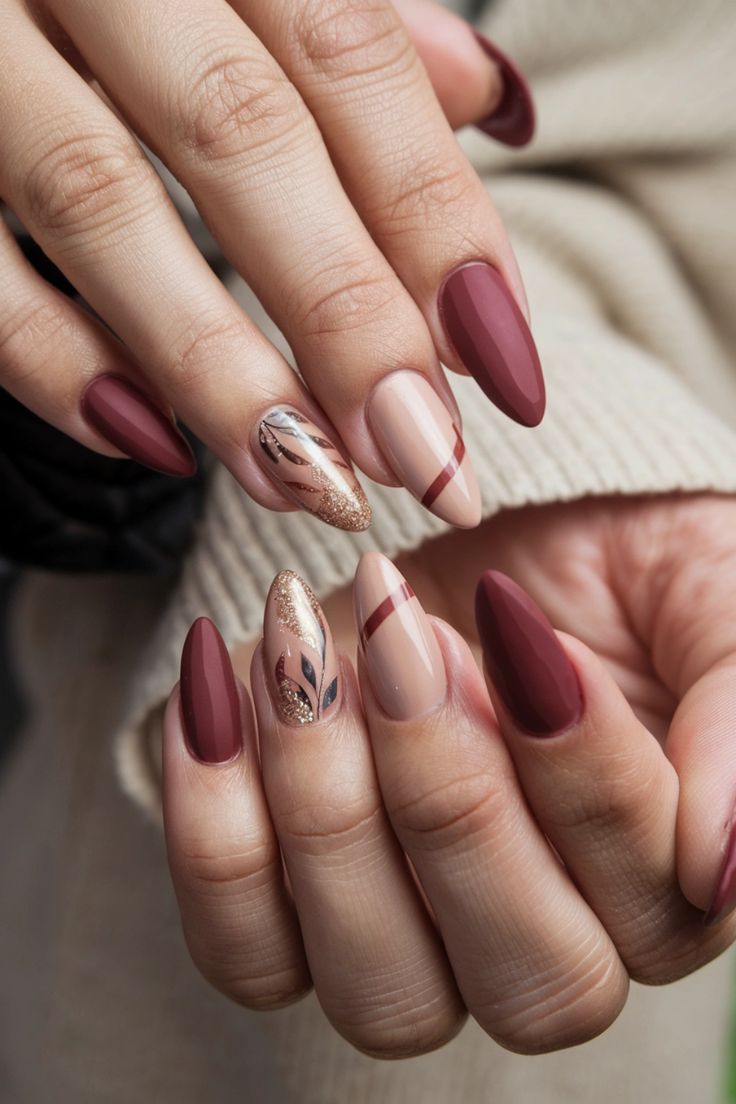 Chic Nail Design: Deep Burgundy and Nude with Gold Accents and Leaf Patterns.