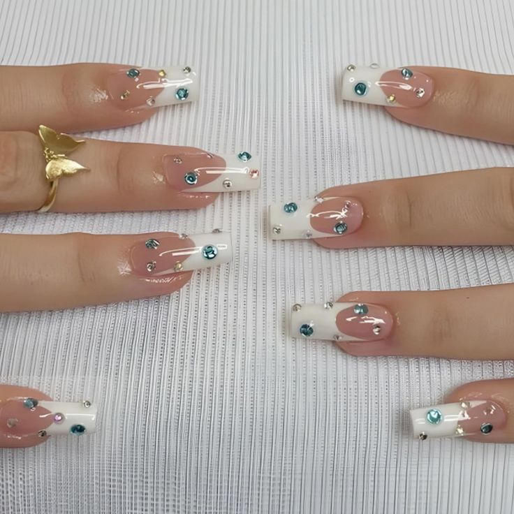 Sophisticated Nail Design: Soft Pink and Classic White Tips with Shimmering Blue Gemstone Embellishments.