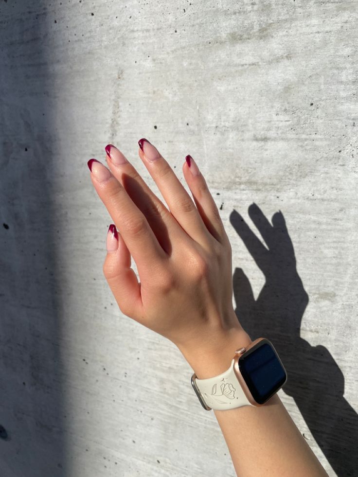 Chic Gradient French Manicure with Deep Red Tips Against a Textured Backdrop.