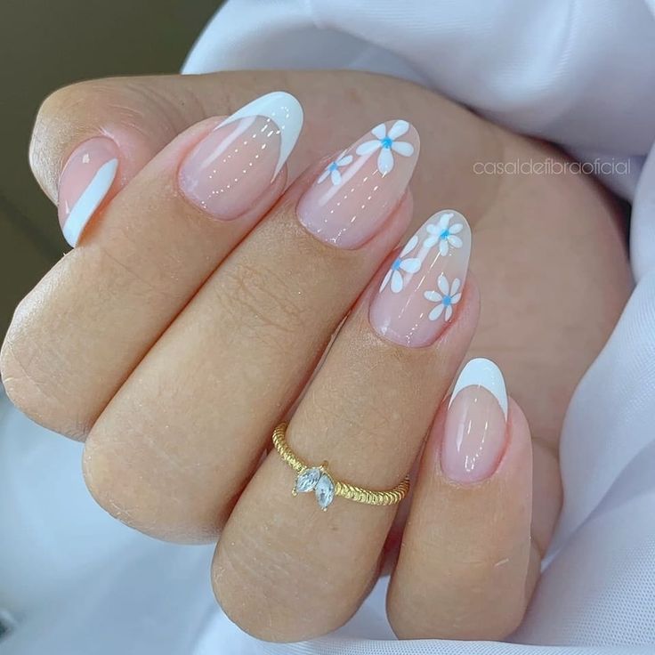 Elegant Floral Nail Design: Soft White Tips and Delicate Blue Flowers with a Nude Base and Gold Accents.