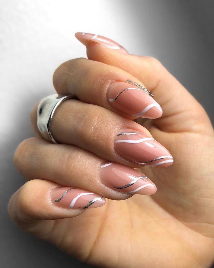 Chic Almond-Shaped Nails: Nude Base with White Swirls and Metallic Silver Accents.