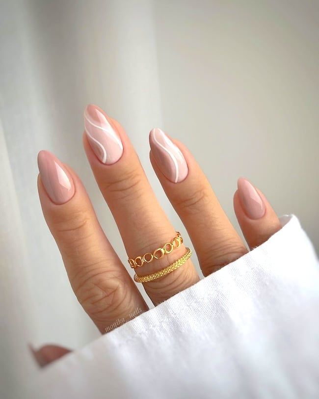 Soft Nude Almond Nail Design with Delicate White Swirls and Gold Accents.