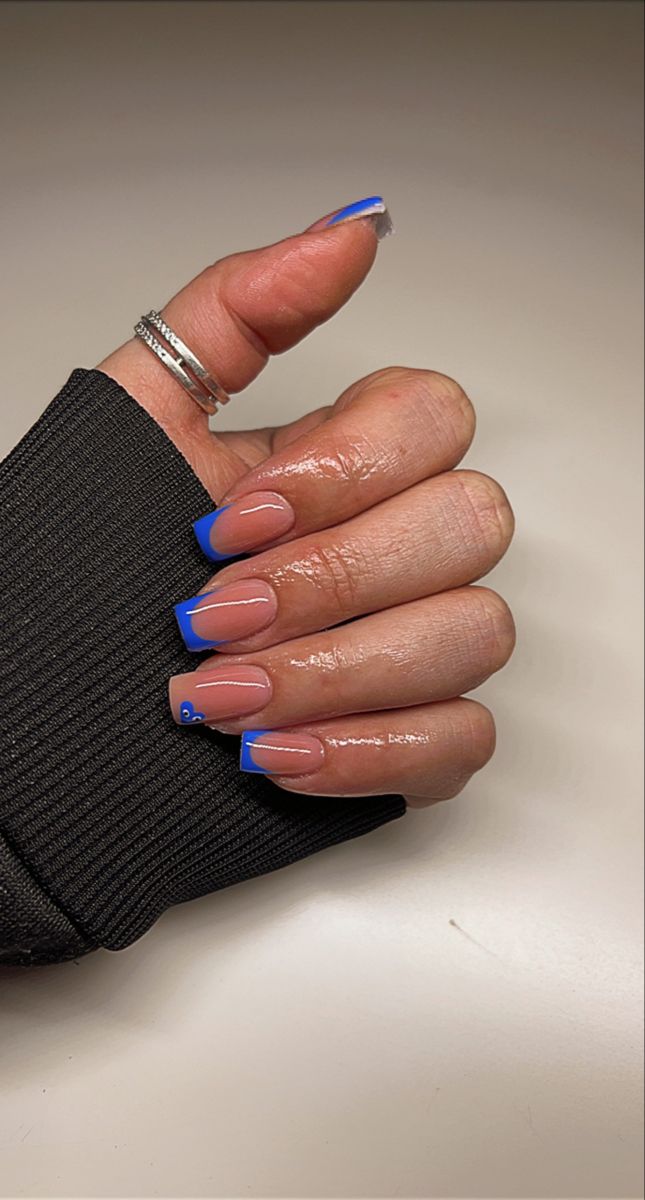 Stylish Nude and Vibrant Blue French Tip Nail Design with Playful Heart Accents.