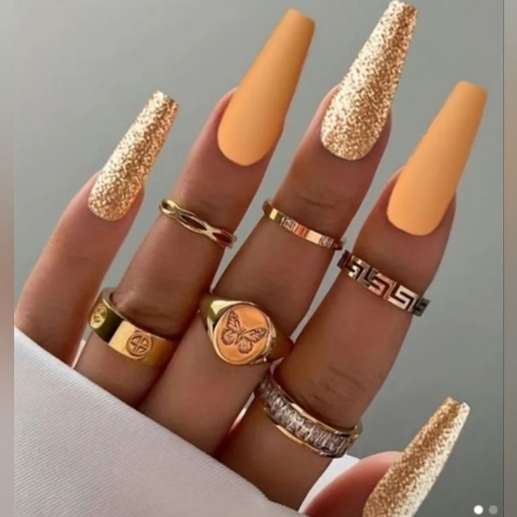 Chic Almond-Shaped Nails: Glossy Peach with Sparkling Gold Tips and Elegant Rings.