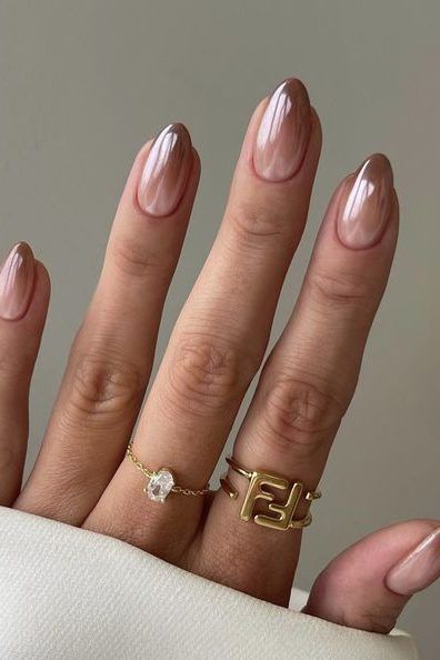 Elegant Almond-Shaped Manicure with Chic Nude Polish and Trendy Gold Ring Accents.