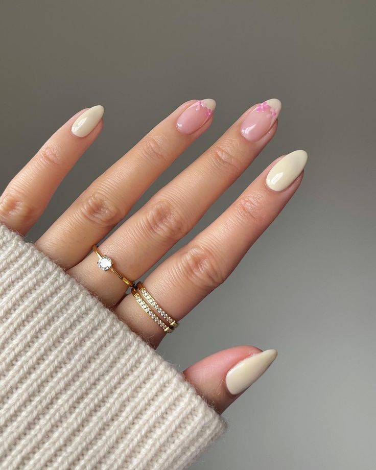 Chic Almond-Shaped Nail Design in Neutral Tones with Floral Accents and Minimalist Gold Rings.