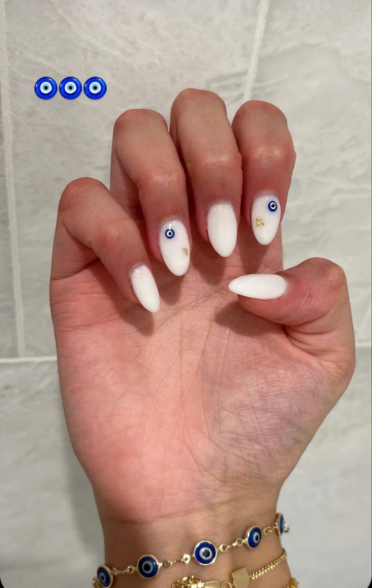 Chic Glossy White Nail Design with Pointed Tips and Evil Eye Accents, Paired with a Delicate Bracelet.