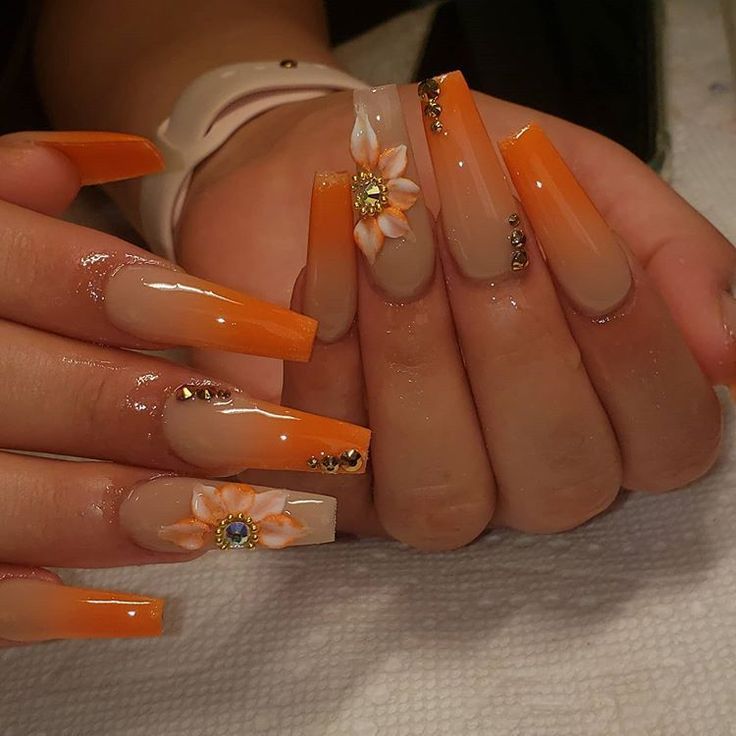 Sophisticated Orange and Nude Gradient Nail Design with Floral Accents and Gem Details.