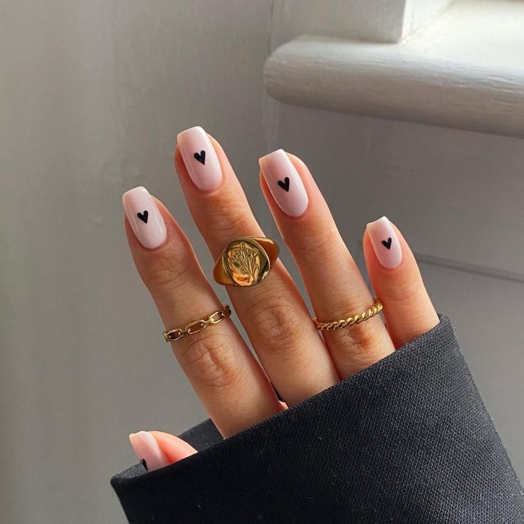 Elegant Chic Manicure: Soft Pink Nails with Black Hearts and Gold Accents.