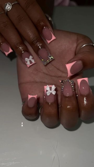 Chic Nail Design: Soft Pink Shades with White Bows and Rhinestones for a Trendy Look.