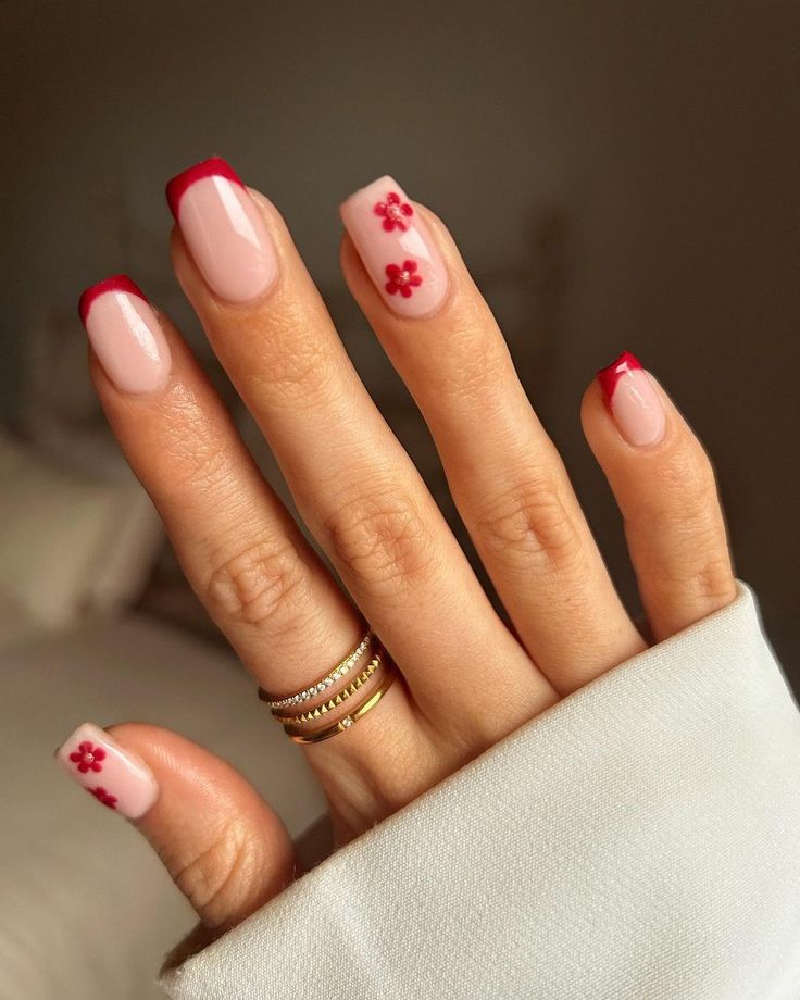 Chic Soft Pink Nail Design with Bold Red French Tips and Floral Accents.