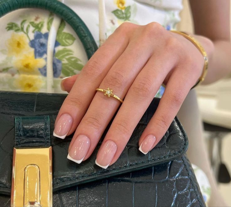 Chic French Tip Manicure Enhanced by Delicate Gold Accessories and a Stylish Green Handbag.