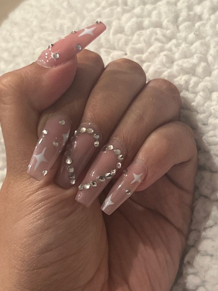 Elegant Soft Pink Nail Design with Elongated Tips, Star Patterns, and Rhinestones.