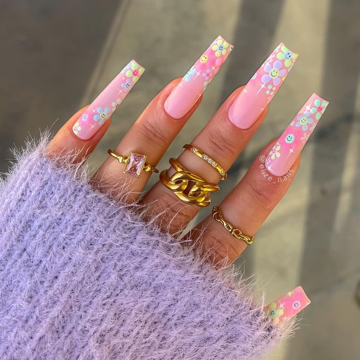 Trendy Pastel Pink Acrylic Nails with Vibrant Floral Designs and Gold Ring Accents.